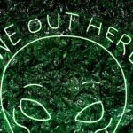 Green neon alien head with text "we out here"